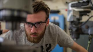 A student is working at a drill station in the NMT Mechanical Engineering Machine Shop.